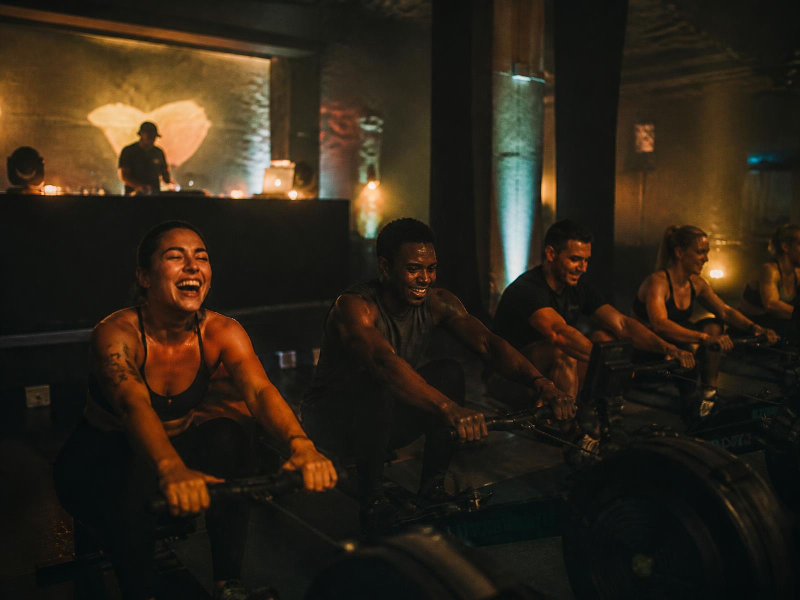 People rowing together at a Peak Watt Club pop-up with a DJ in the background